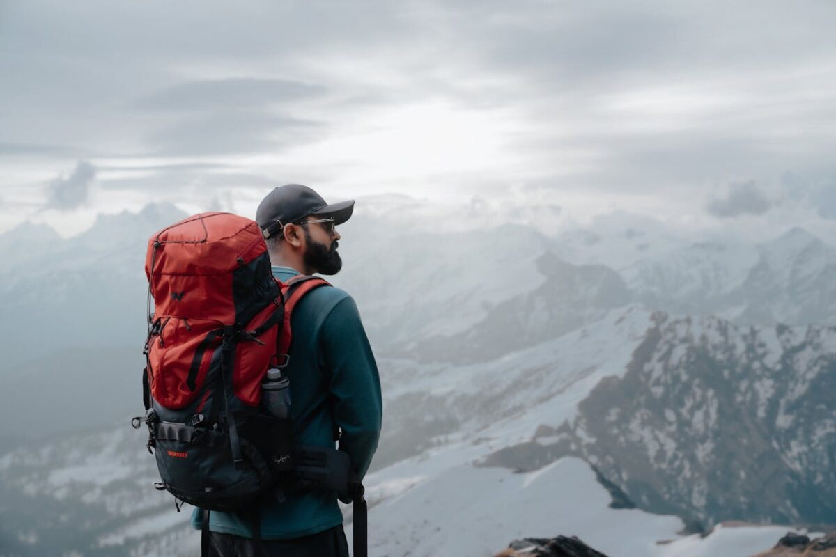 An adventurous male hiker with a red backpack enjoying the stunning mountain view at sunrise.